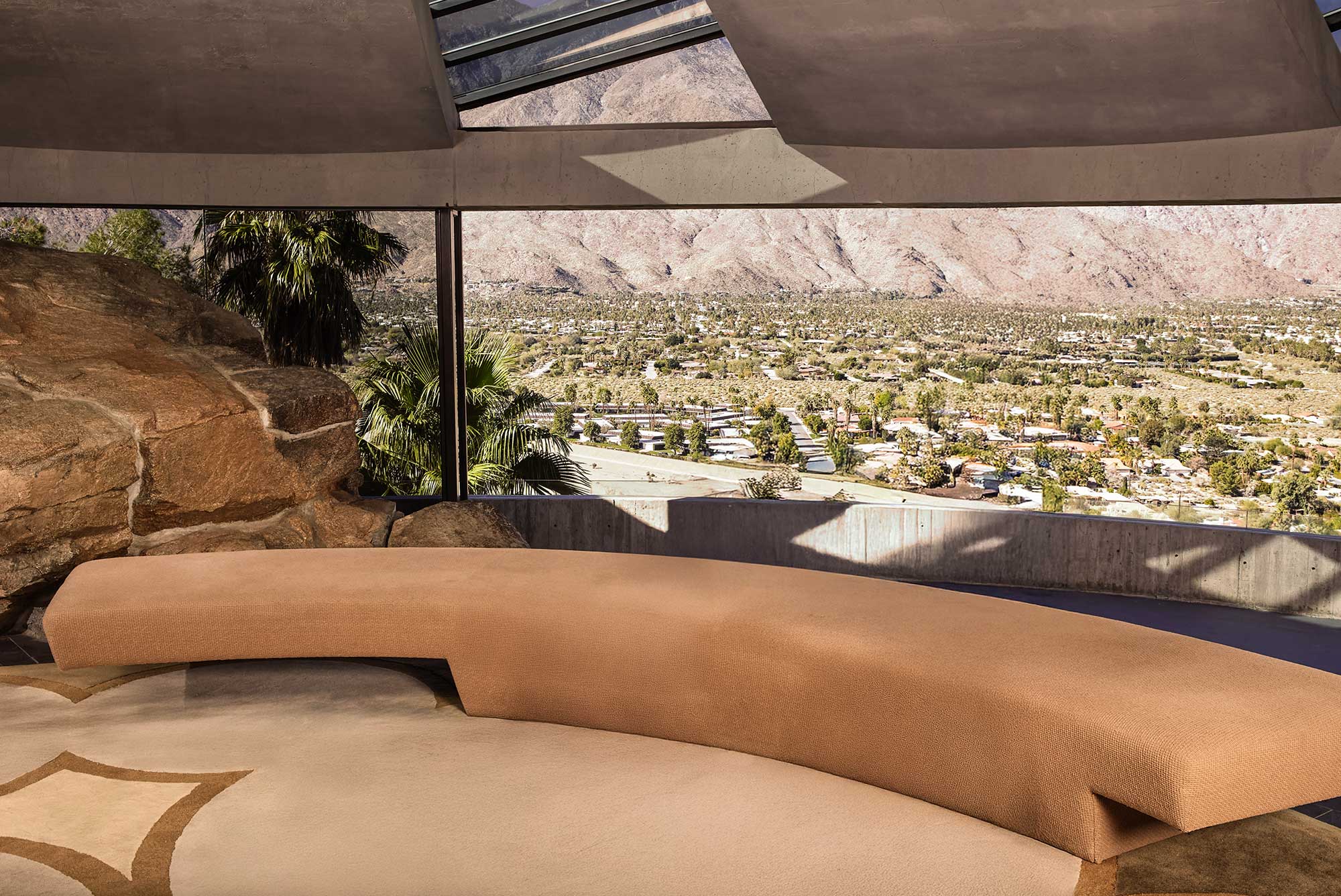 Interior of the Elrod House in Palm Springs showing the concrete dome with alternating glass segments, integrated boulders, curved sofa, and panoramic view of the Coachella Valley